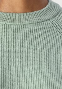 Grüner gerippt gestrickter Pullover mit Rundhalsausschnitt und strukturiertem Oberflächen, ausgestattet mit langen Raglanärmeln und einem weichen, gemütlichen Gefühl.