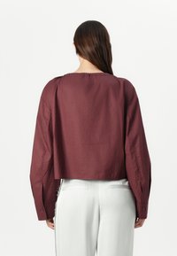 Maroon cropped shirt with long sleeves, a wide neckline, and buttoned cuffs, made from a smooth, textured fabric.
