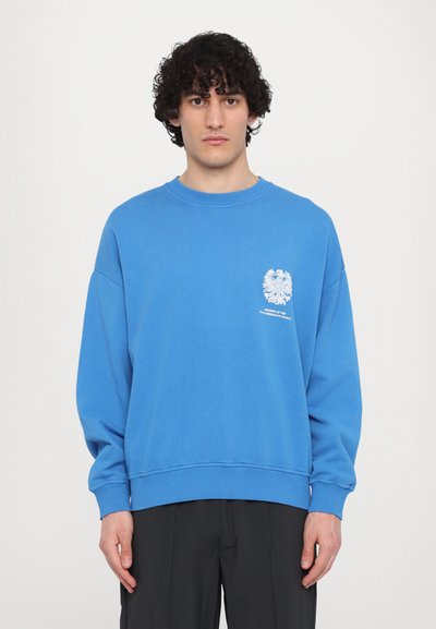 Blaues Sweatshirt mit Rundhalsausschnitt und langen Ärmeln. Mit einem weißen grafischen Emblem auf der linken Brust. Weicher Baumwollstoff.