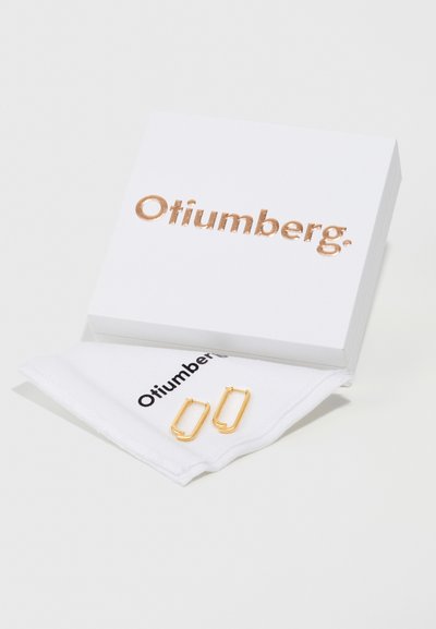 Gulde rektangulære hoopearrings på et hvidt klæde, præsenteret i en hvid æske med et skinnende rosaguld "Otiumberg" logo præget på toppen.