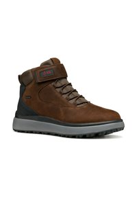 Bottines en daim marron avec une semelle en caoutchouc grise, dotées d'un système de laçage, d'une sangle ajustable et d'accents en panneaux texturés.