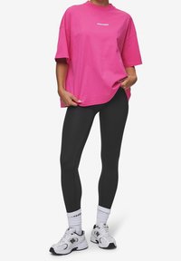 Rosa oversized t-shirt med rund halsringning och korta ärmar, tillsammans med svarta leggings och vita sportskor.