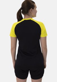 T-shirt sportiva nera e gialla con colletto rotondo e maniche corte raglan, realizzata in tessuto leggero, abbinata a pantaloni corti neri.