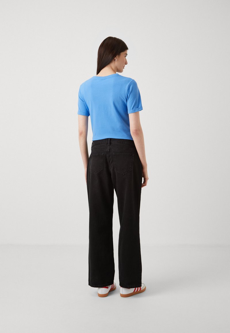 Blauw T-shirt met korte mouwen gecombineerd met zwarte wijde broek, voorzien van achterzakken en een soepele textuur. Sneakers met rode accenten.