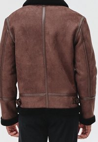 Giacca in shearling marrone con una texture morbida, cuciture orizzontali e colletto nero. Presenta cinturini in vita per la regolazione.