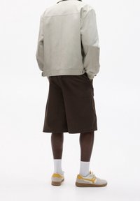 Chaqueta gris, pantalones cortos marrones, zapatillas blancas y amarillas. Tela suave, corte holgado, pantalones cortos hasta la rodilla y bolsillos discretos en los pantalones cortos.