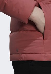 Puchowa kurtka w kolorze burgundowym, wykonana z gładkiego, lekkiego materiału. Zawiera boczną kieszeń oraz detal z logo na dolnym brzegu.