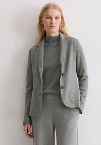 Veste grise à fines rayures avec deux poches avant, fermeture à un bouton, et col roulé gris assorti. Texture douce, coupe ajustée.