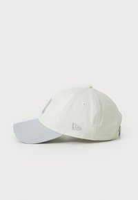 Baseball cap med en lysebeige krop og grå skygge, med broderede accenter og ventilationshuller langs kronen.