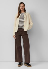 Crème kleurige ribgebreide cardigan met knopen, gestreept zwart-wit topje, bruine wijde broek en zwarte platform schoenen. Eenvoudige, gelaagde outfit.