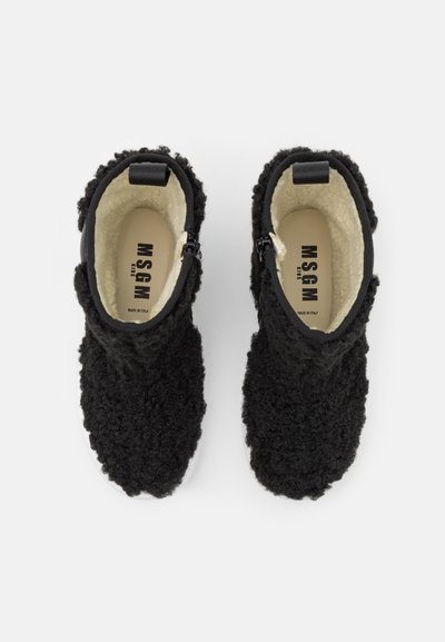 Botas de tornozelo pretas e peludas com um exterior texturizado e forro interior branco. Apresentam um fecho de correr para fácil calçar e uma base preta sólida.