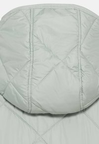 Veste matelassée vert clair avec capuche ajustée, motifs de coutures diagonales et texture lisse.