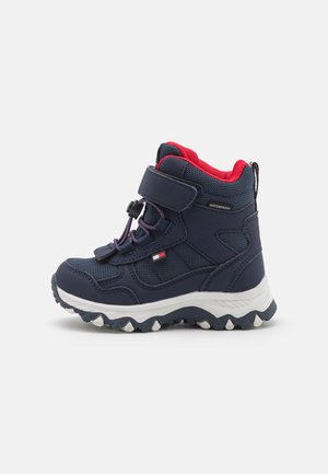 Bottes de randonnée imperméables bleu marine et rouge avec fermeture velcro, lacets élastiques et semelle blanche robuste rainurée conçues pour enfants.