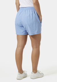 Pantaloni corti azzurri chiari con vita elastica, tasche laterali e un tessuto leggero, abbinati a scarpe da ginnastica bianche.