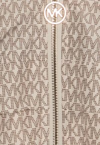 Beige jacka med ett upprepat mönster av ljusbruna 'MK'-logotyper. Centrerad dragkedja med metalliska detaljer. Mjuk, texturerad tyg.