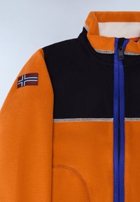 Fleec jakna s narančastim tijelom, crnim ramenima, plavim patentnim zatvaračem i zakrpom norveške zastave na lijevoj ruci. Glatka tekstura, dizajn s punim patentnim zatvaračem.