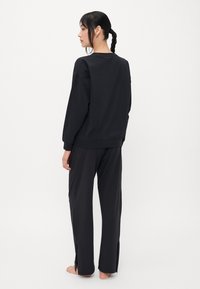 Zwarte sweatshirt en bijpassende broek set, met een losse fit, ronde halslijn en zijsplitten aan de onderkant van de broek. Zachte textuur.