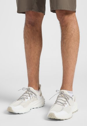 Mesh-Laufschuhe in hellem Beige und Weiß, mit einer strukturierten Oberseite, Schnürverschluss und einer dicken, gepolsterten Sohle mit rutschfestem Muster.