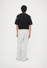 Czarny t-shirt z krótkim rękawem z logo na rękawach, w połączeniu z szarymi dresami z elastycznym paskiem i bocznymi kieszeniami.