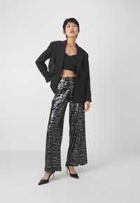 Fekete cropped top blézerrel, fűzős részletekkel; fényes, széles szárú nadrág szürke mintával; fekete magassarkú neon zöld kiegészítőkkel.