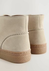 Bottines en suède beige avec une semelle en caoutchouc texturé couleur tan, présentant une finition lisse et de subtils détails de couture le long des coutures.
