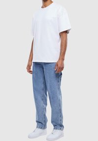 Camiseta de algodón blanca, corte holgado, cuello redondo. Jeans de mezclilla azul claro, estilo relajado con bolsillos laterales. Zapatillas blancas.