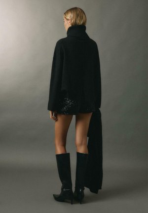 Črn, prevelik pulover s fizičnim ovratnikom, rebrasto teksturo, v kombinaciji s sijočimi črnimi šortami iz bleščic in črnimi usnjenimi škornji do kolen.