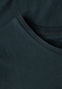 Tmavě zelená bavlněná tkanina s hladkou texturou, se zakulaceným výstřihem a žebrovanými detaily kolem límce.