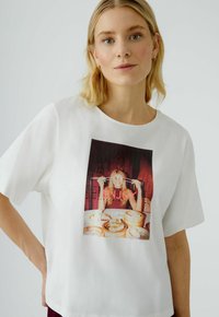 Witte T-shirt met korte mouwen met een kleurrafisch van een persoon die eetstokjes vasthoudt en geniet van eten, met het woord "ENJOY" gedrukt.