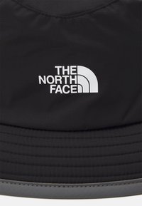 Cappello a secchiello nero realizzato in un tessuto resistente, con una visiera testurizzata e un logo bianco di "The North Face" sulla parte anteriore.