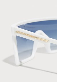 Vita solglasögon med geometrisk design, blåa gradientlinser och en gulddetalj på bågen med varumärket "Carrera."