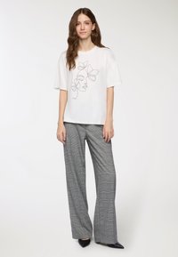 Biała koszulka z krótkim rękawem z czarnym szkicowym rysunkiem twarzy i kwiatów, w połączeniu z szarymi szerokimi spodniami w kratę i czarnymi spiczastymi butami.