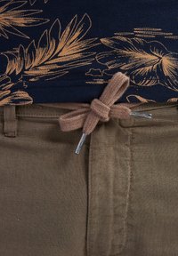 Camicia blu navy con motivo floreale dorato al colletto, cordoncino beige annodato in vita, e pantaloni marrone chiaro con dettagli con zip.