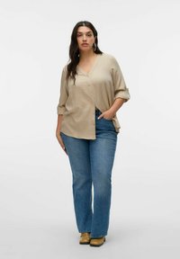 Beige overhemd met knopen en een v-hals, met opgerolde mouwen, gecombineerd met blauwe flare jeans en bruine schoenen. De stof lijkt textuur te hebben.