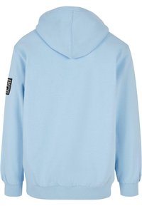 Světlomodrá mikina s kapucí a dlouhými rukávy, s černo-bílou nášivkou na levém horním rukávu, zobrazená zezadu.