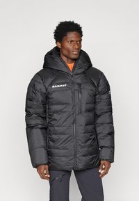 Casaco puffer preto com capuz ajustável, design acolchoado, fecho frontal com zíper, logótipo no peito e acabamento texturizado.
