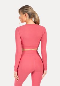 Top cropped a maniche lunghe in tessuto rosa uniforme con un design aderente e una texture liscia, abbinato a leggings a vita alta coordinati.