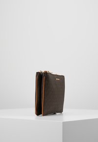 Hnědá kožená crossbody taška s texturovaným vzorem, zlatými kovovými prvky a kontrastními béžovými akcenty; zapínání na zip na vrchu.