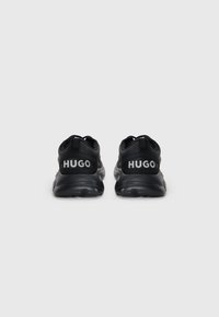 Svart sneakers med teksturert overdel, som har en polstret krage og "HUGO"-merke på hælen, samt en gummisåle for godt grep.