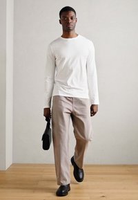 Balta ilga rankovė marškiniai, šviesiai bežinės kelnės, juodi batai, laikantis juodos kuprinės. Paprastas dizainas su lygiu paviršiumi ir laisvu fasonu.