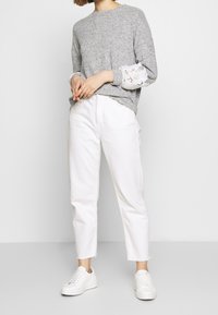 Grå tröja med spetsdetaljer på ärmarna, ihop med vita raka jeans och vita sneakers. Enkelt design och avslappnad outfit.