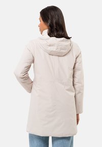 Helle beige wasserfeste Jacke mit Kapuze, entspannter Schnitt, langen Ärmeln und glatter Textur. Nahtdetails sind am Rücken sichtbar.