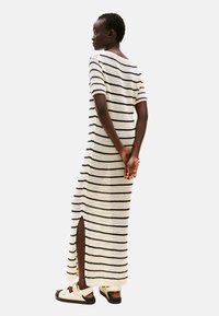 Sukienka maxi na szydełku w paski w kolorze kremowym i granatowym z krótkimi rękawami, z bocznym rozcięciem i luźnym krojem, zestawiona z lekkimi sandałami.