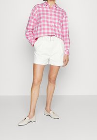 Růžovo-bílá kostkovaná košile na knoflíky, bílé plisované šortky a smetanové mokasíny se zlatým akcentem. Hladký materiál, volný střih.