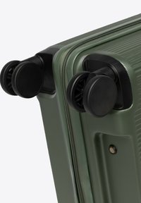 Detailní záběr rohu zeleného kufru s tvrdou skořápkou, ukazující dvě sady černých dvojitých koleček a texturovaný povrch.