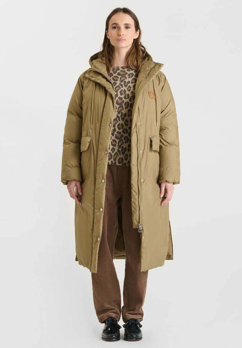 Olijfgroen lange pufferjas met een capuchon, voorzakken en knoopsluiting, gecombineerd met een trui met luipaardprint en bruine gebreide broek.