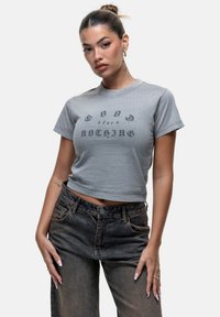 T-shirt grigia corta con testo stampato nero "GOD for NOTHING", scollatura tonda, maniche corte e morbido cotone. Indossata con jeans scuri.