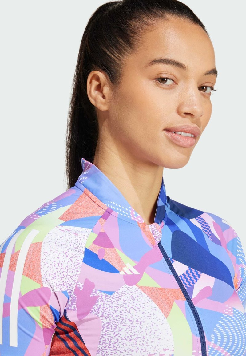 Bunte Sportjacke mit einer Mischung aus geometrischen Mustern in Pink, Blau und Grün, mit einem Reißverschluss und hohem Kragen.