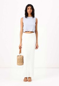 Top cropped canelado azul claro com decote redondo, combinado com uma saia longa branca texturizada. Segurando uma bolsa redonda de palha.