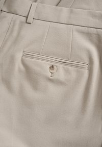 Pantalons beiges en tissu lisse et texturé. Dotés d'une poche arrière avec fermeture à bouton et de détails de couture verticale.